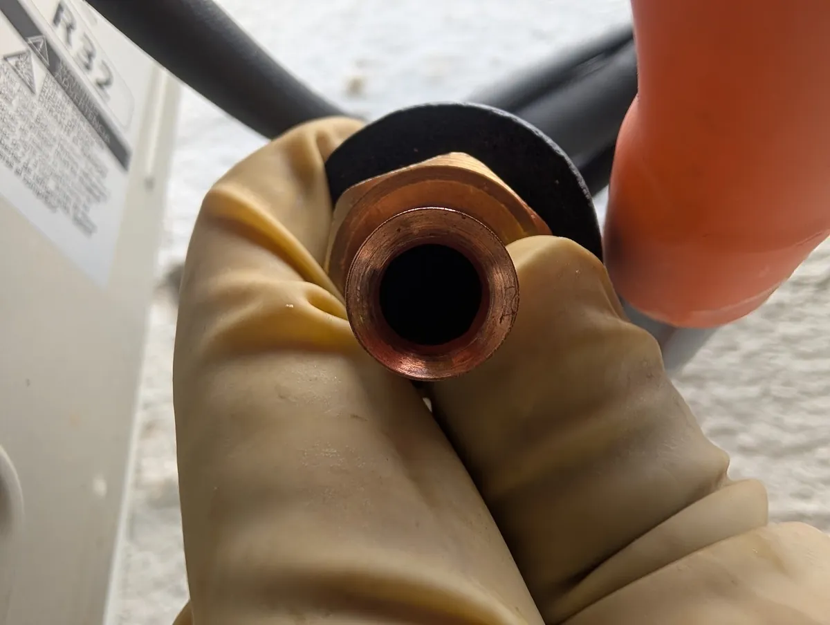 Gloved hand holding a copper flare fitting on the line set of an R-32 mini-split system